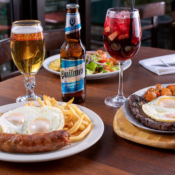 Argentinian meal with steak, fried eggs, sausage, fries, salad, Quilmes beer, and sangria.