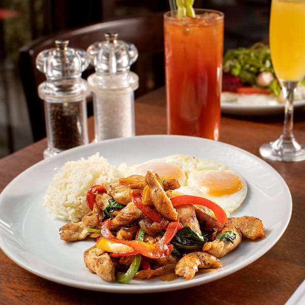 Chicken and peppers with rice and two fried eggs, with drinks and salt/pepper shakers.