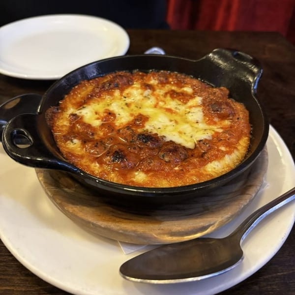 A bubbling, cheesy provoleta in a cast iron pan, served on a wooden trivet with a spoon.