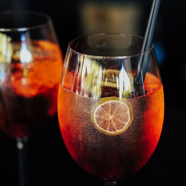 Two frosty glasses of red cocktails with lemon slices and straws, against a dark background.