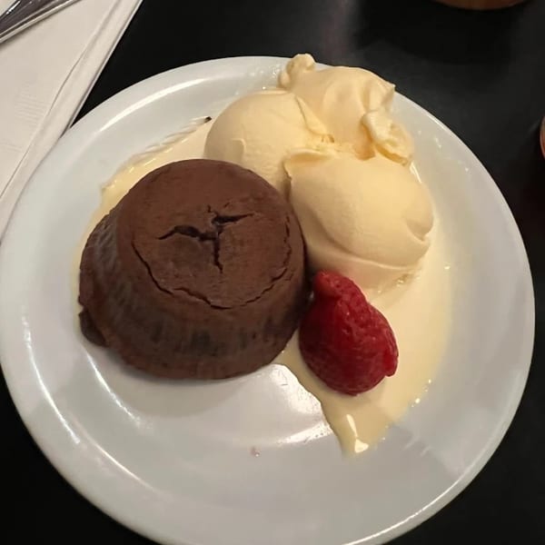 A chocolate lava cake with two scoops of vanilla ice cream and a strawberry on a white plate.