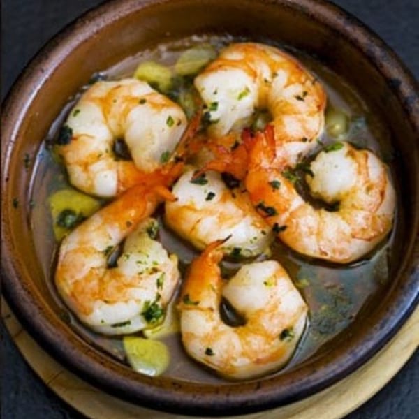 Shrimp scampi in a brown ceramic bowl, garnished with green herbs and garlic.