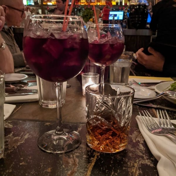 Two glasses of red sangria and a glass of whiskey on a dark table at Buenos Aires.