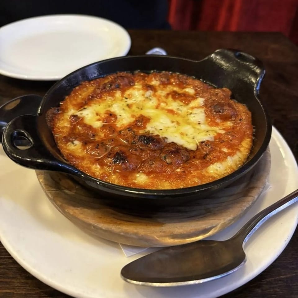 A cast iron skillet of bubbling, cheesy provoleta with a spoon on a white plate.