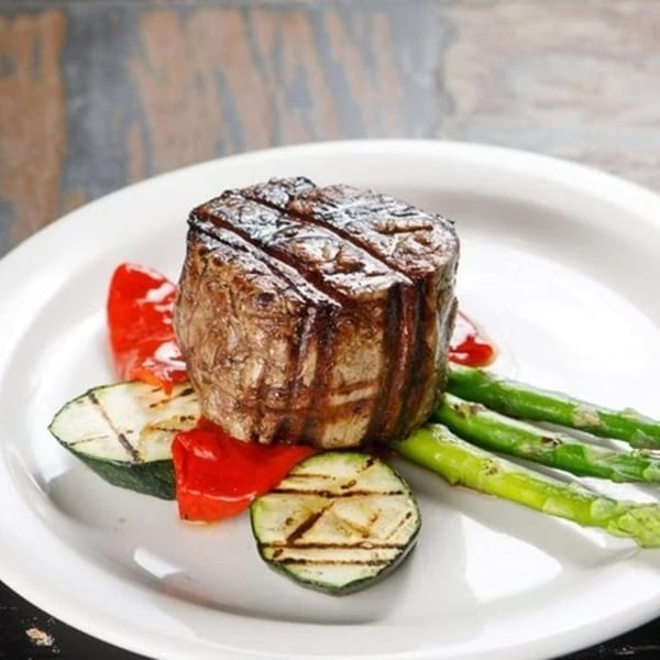 Grilled Argentinian steak with asparagus, zucchini, and red bell peppers on a white plate.