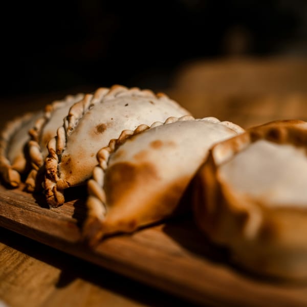 Close-up of several golden-brown Argentinian empanadas with crimped edges on a wooden board.
